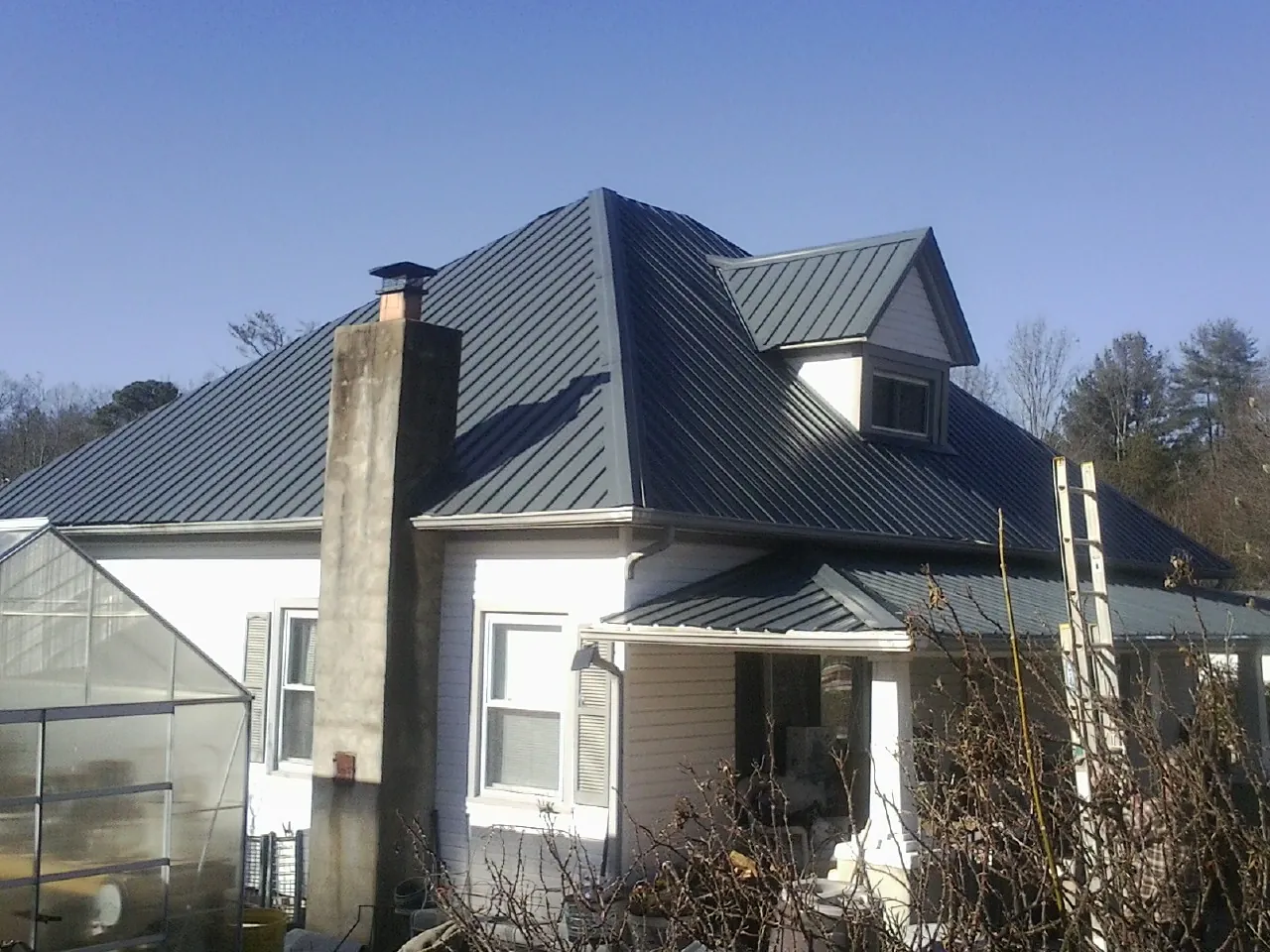 Dark blue standing seam metal roof on a white farmhouse with dormer — Slate & Tile Roof Repair by Roofing Brothers in Southside