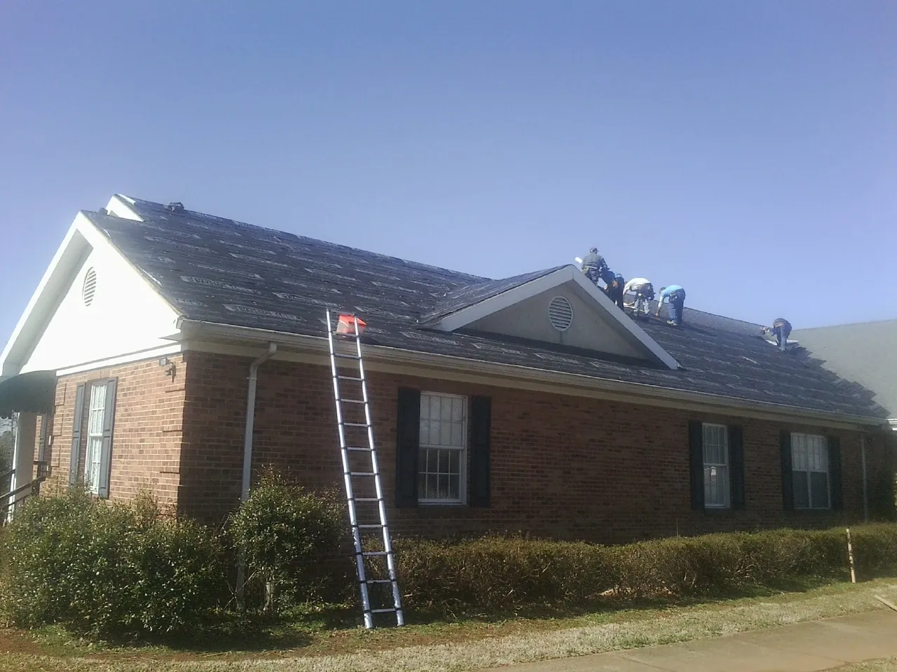 Crew tearing shingles off a brick ranch roof with a ladder set — Emergency Roof Repair work by our crew in Southside