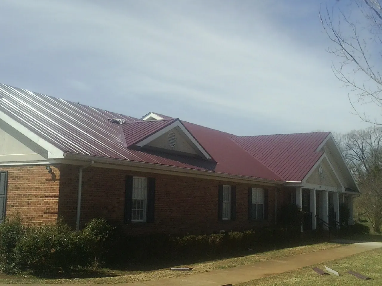 Red metal roof with gabled entries on a long brick building, from a Hail Damage Roof Repair job in Southside