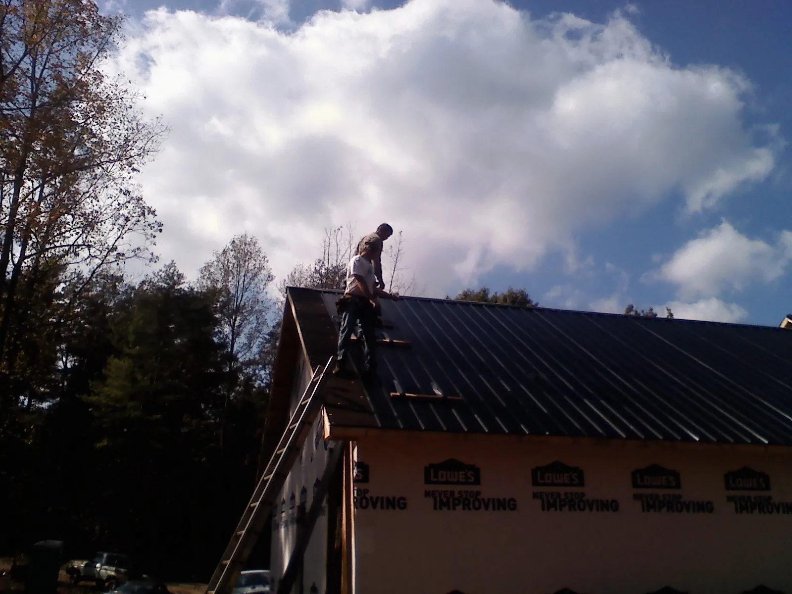 Roofer fastening dark metal panels high against a cloudy sky, from a Roof Inspection job in Southside