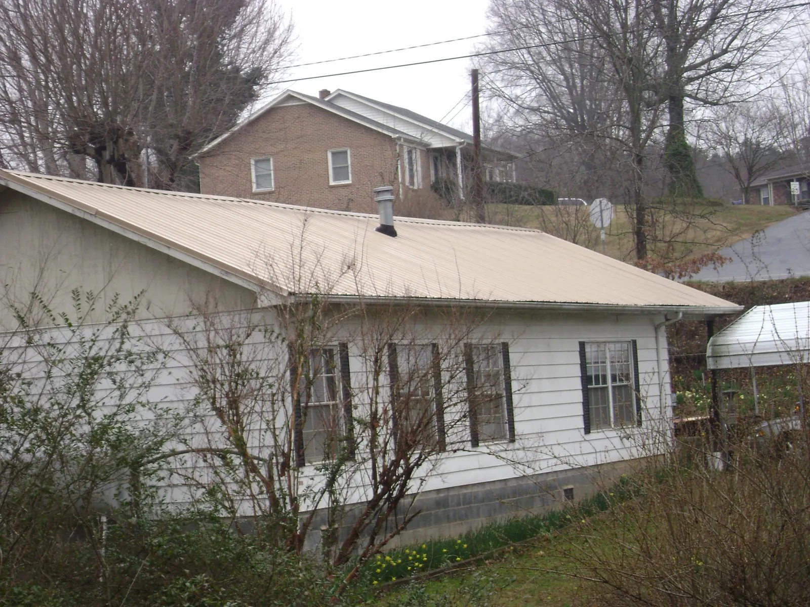 Tan metal roof on a white sided house set into a hillside — Commercial Roofing by Roofing Brothers in Southside