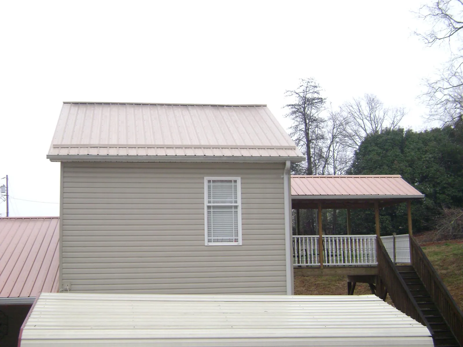 Tan metal roofs on a two story addition and attached porch, from a Roof Replacement job in Southside